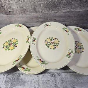 Peut inclure: Quatre plats de service ovales blanc cassé avec un motif floral. Le centre de chaque plat présente un groupe de feuilles jaunes et vertes avec des baies violettes et rouges. Des feuilles et des baies vertes sont également sur les bords.