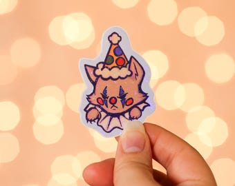 May include: A sticker featuring a cartoon fox dressed as a clown. The fox has a sad expression, wearing a colorful party hat and a ruffled collar. The sticker has a holographic effect.