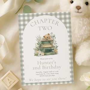 May include: A baby-themed invitation card with a grey gingham border. The card features the text "CHAPTER TWO" and "Hunter's 2nd Birthday." A teddy bear sits atop a stack of books, surrounded by greenery. Wooden alphabet blocks and a teddy bear are also visible.