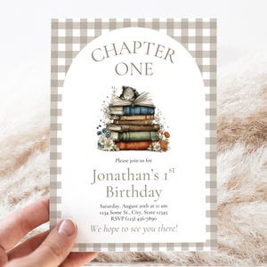 May include: A rectangular invitation card with a beige and white gingham border featuring an arched white center. It displays the text CHAPTER ONE, an illustration of a bear sleeping on a stack of books, and Jonathan’s 1st Birthday details.