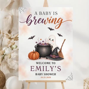May include: A rectangular sign featuring the text A BABY IS brewing, WELCOME TO EMILY'S BABY SHOWER, and 10.25.2026. The design includes a black cauldron, a pumpkin, a ghost, a witch hat, a broom, and bats on a white background with spider webs.