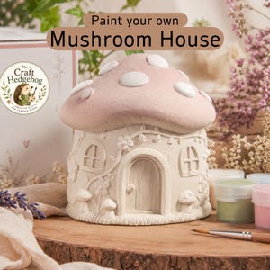 May include: A paint-your-own mushroom house craft kit featuring a beige ceramic structure with a pink cap and white spots. The house has a central arched door, two windows, and small sculpted mushrooms. Includes paint pots and a paintbrush.