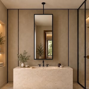 May include: A rectangular bathroom vanity with a beige stone countertop and integrated sink, featuring a black faucet and handles. Above, a tall, thin, black-framed mirror hangs from a ceiling-mounted rod against a smooth, light brown wall.