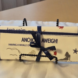 Peut inclure: Un organisateur enroul&eacute; sur le th&egrave;me nautique, avec un ruban et une bordure bleu marine. Le tissu cr&egrave;me pr&eacute;sente des phrases comme "Anchor Aweigh!" et des illustrations de sir&egrave;ne, de mouettes et de bou&eacute;e de sauvetage.