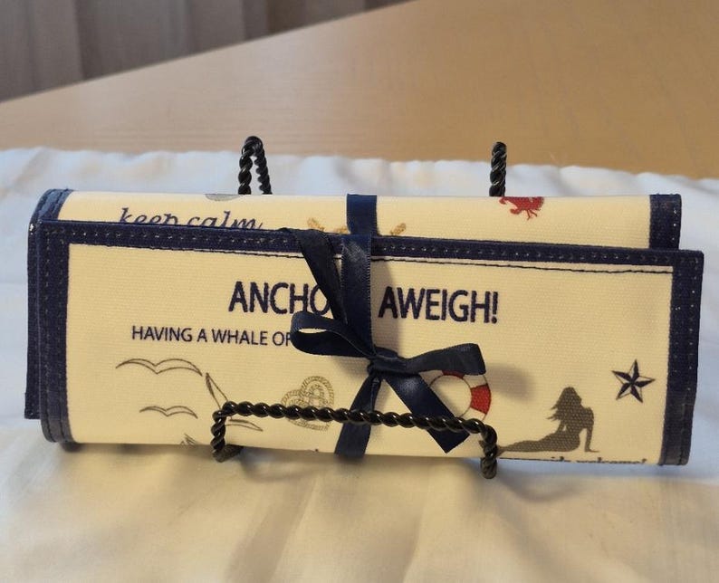 Peut inclure: Un organisateur enroul&eacute; sur le th&egrave;me nautique, avec un ruban et une bordure bleu marine. Le tissu cr&egrave;me pr&eacute;sente des phrases comme "Anchor Aweigh!" et des illustrations de sir&egrave;ne, de mouettes et de bou&eacute;e de sauvetage.