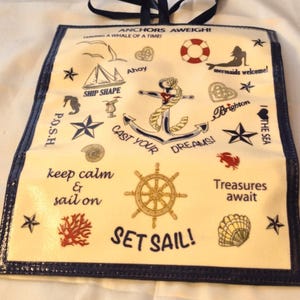 Peut inclure: Un sac fourre-tout sur le th&egrave;me nautique avec une bordure et des poign&eacute;es bleu marine. Le tissu cr&egrave;me pr&eacute;sente diverses illustrations marines, dont une ancre, un gouvernail et des &eacute;toiles de mer, ainsi que des phrases comme "Cast Your Dreams!" et "Set Sail!"