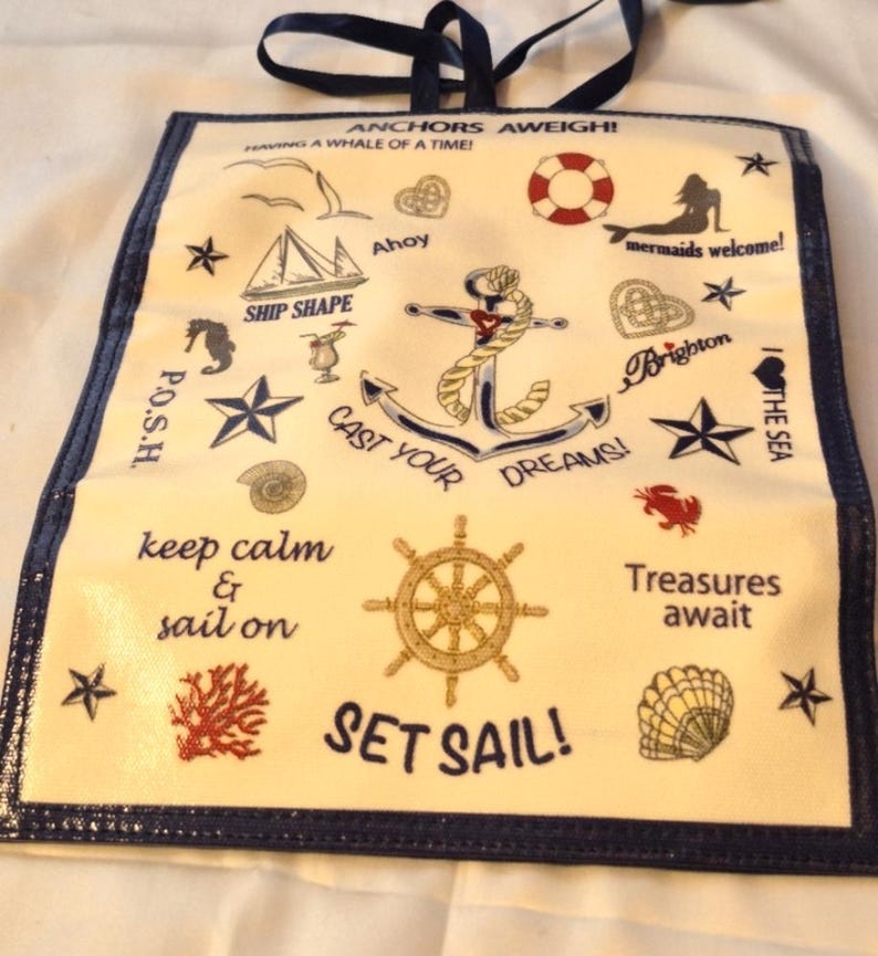 Peut inclure: Un sac fourre-tout sur le th&egrave;me nautique avec une bordure et des poign&eacute;es bleu marine. Le tissu cr&egrave;me pr&eacute;sente diverses illustrations marines, dont une ancre, un gouvernail et des &eacute;toiles de mer, ainsi que des phrases comme "Cast Your Dreams!" et "Set Sail!"