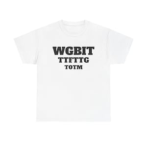 May include: White t-shirt with the text "WGBIT TTFTTG TOTM" printed in black. The shirt is a classic crew neck style, suitable for casual wear. The text is centered on the chest.