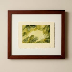 May include: A framed watercolor painting with a dark brown wooden frame. The artwork features a landscape scene in shades of green and yellow, with a textured, torn-edge paper. The painting is mounted on a white mat.