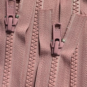 May include: Close-up of four pink zipper tapes with metal sliders. The zippers have a textured, woven appearance.