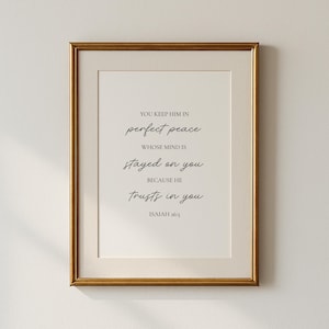 May include: A framed print with a gold-colored frame. The print features the text "YOU KEEP HIM IN perfect peace WHOSE MIND IS stayed on you BECAUSE HE trusts in you ISAIAH 26:3" in a black, elegant font on a white background.