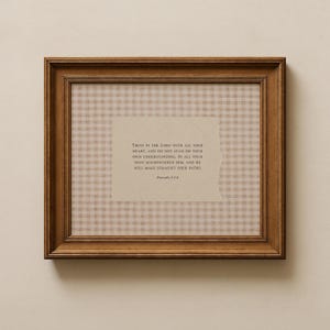 Op de afbeelding: Een ingelijste print met een bruine houten lijst. De print heeft een beige ruitpatroon en een centraal rechthoekig stuk papier met tekst uit Spreuken 3:5-6. De tekst luidt: "Vertrouw op de Heer met heel je hart..."