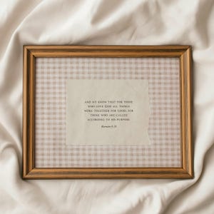 May include: A framed print with a gold-toned wooden frame. The print features a beige and white gingham pattern background with a torn paper overlay. The text reads, "AND WE KNOW THAT FOR THOSE WHO LOVE GOD ALL THINGS WORK TOGETHER FOR GOOD..." Romans 8:28.