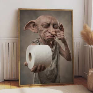 May include: A framed wall art print featuring a wrinkled, large-eared creature with light brown skin wearing a simple, tattered garment. The creature is holding a roll of white toilet paper in one hand while touching its nose with the other hand.