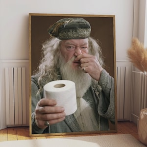 May include: A framed wall art print featuring an elderly person with a long white beard and hair, wearing a dark green cap and robe. The person holds a roll of white toilet paper in one hand while pinching their nose with the other hand.