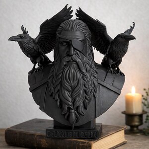 May include: A black bust sculpture of a bearded man with an eye patch, flanked by two ravens. The sculpture sits atop a rectangular base, placed on a stack of books. A lit candle is in the background.