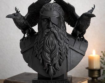 Könnte beinhalten: Schwarze Büste eines bärtigen Mannes mit Augenklappe, flankiert von zwei Raben. Die Skulptur steht auf einem rechteckigen Sockel, der auf einem Stapel Bücher platziert ist. Im Hintergrund eine brennende Kerze.