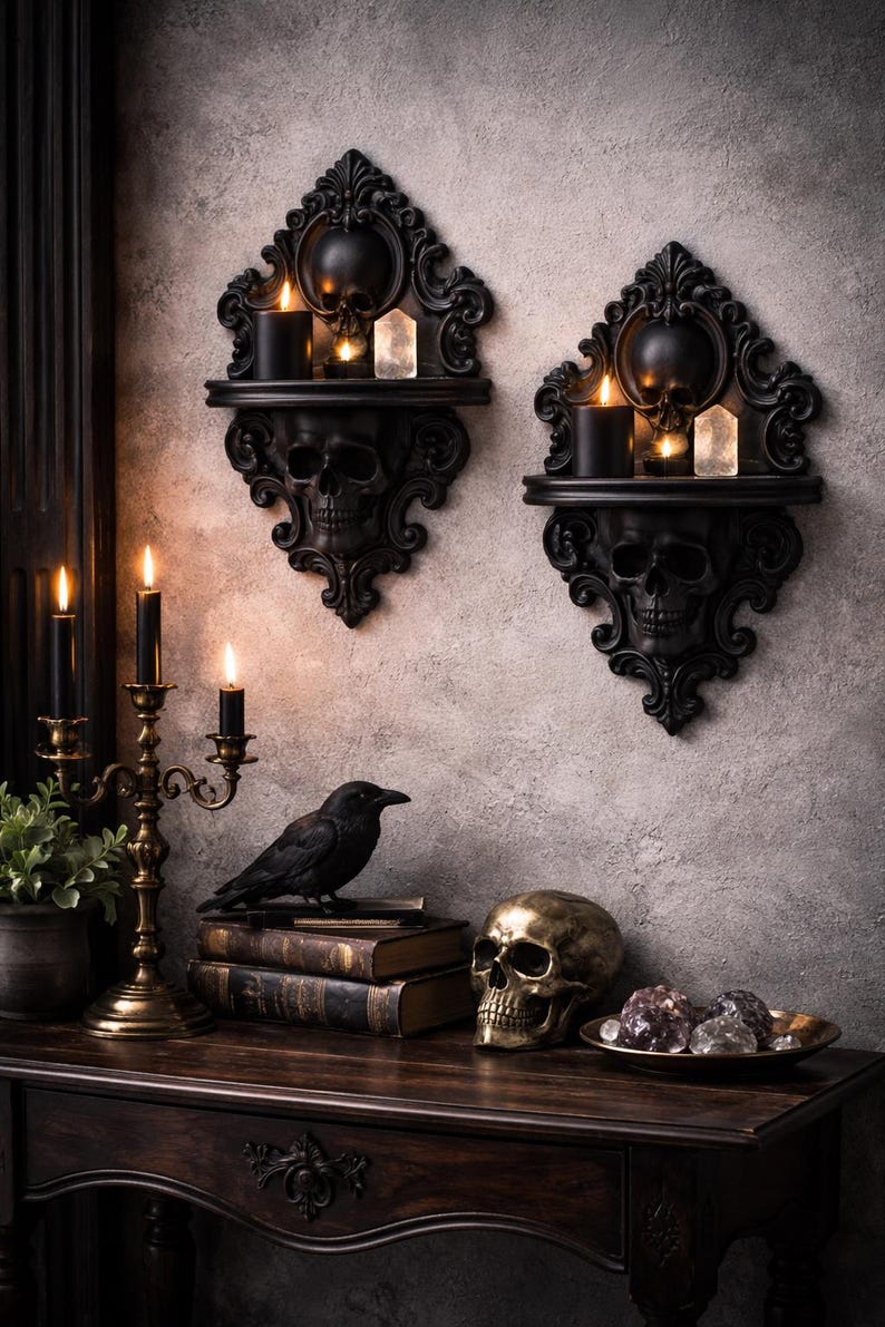 Puede incluir: Decoraci&oacute;n de tem&aacute;tica g&oacute;tica con dos estanter&iacute;as de pared negras con forma de calavera, con velas y cristales. Un candelabro de lat&oacute;n, un cuervo, libros antiguos, una calavera dorada y un cuenco de cristales sobre una mesa de madera oscura.