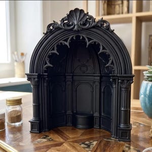 Puede incluir: Una hornacina de exhibición arquitectónica en negro mate con una parte superior arqueada con molduras decorativas de concha, columnas estriadas y un interior empotrado con detalles de paneles. La estructura es independiente y abierta.