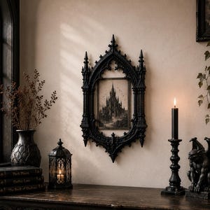 May include: A black ornate gothic-style wall frame featuring a pointed arch design, enclosing a rectangular print of a tall castle. The frame is detailed with vertical columns and pointed finials, mounted on a wall above a dark wooden surface.