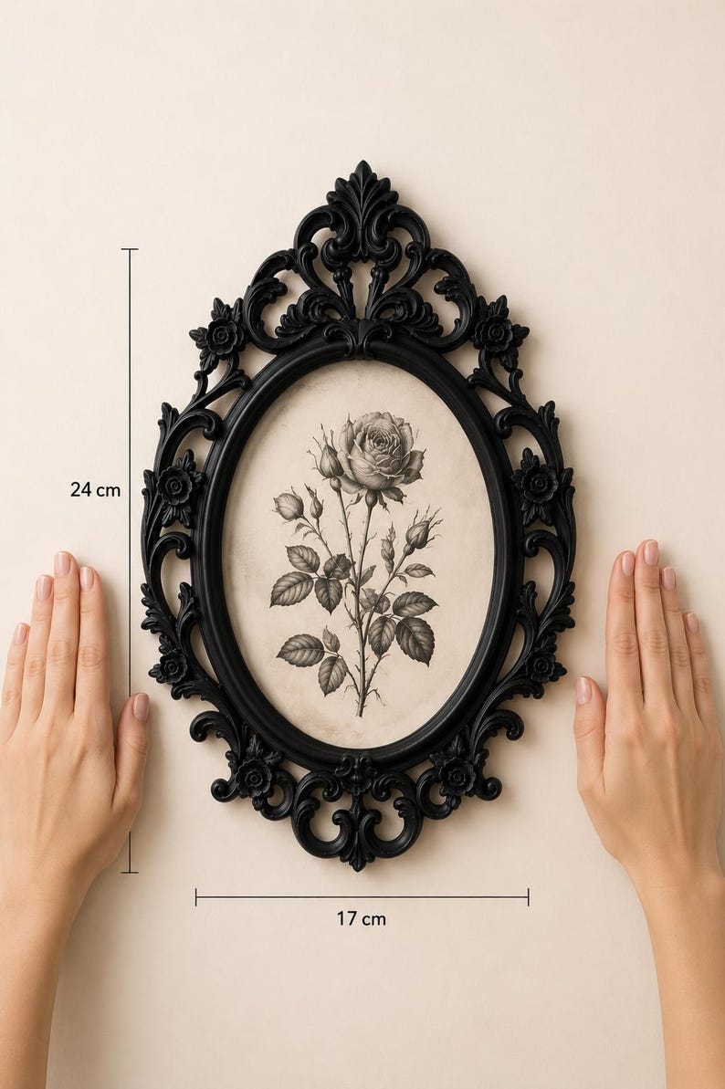 K&ouml;nnte beinhalten: Ein ovaler schwarzer Bilderrahmen mit kunstvollen Schn&ouml;rkeln und floralen Details, der eine schwarz-wei&szlig;e botanische Illustration einer Rose enth&auml;lt. Der Rahmen misst 24 cm in der H&ouml;he und 17 cm in der Breite, wie durch die Messlinien angezeigt.