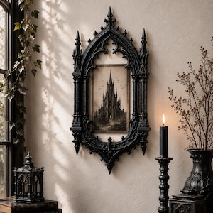 May include: A rectangular wall mirror or frame featuring an intricate black gothic-style border with pointed arches and spires. Inside the frame is a sepia-toned illustration of a tall, dark castle with multiple towers and flying birds.