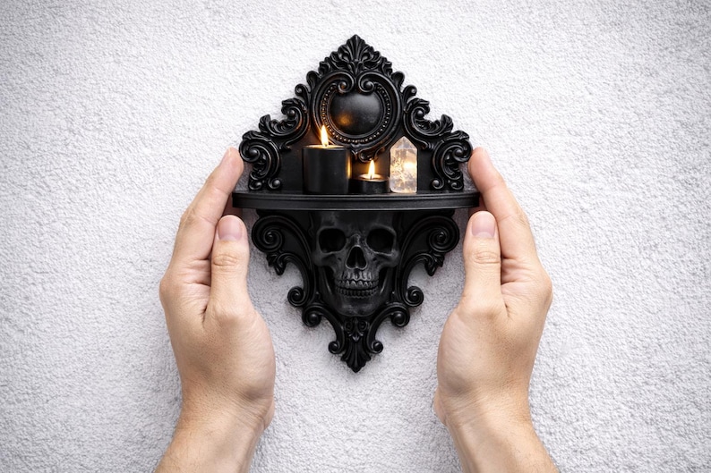 Puede incluir: Estante de pared decorativo negro con dise&ntilde;o de calavera. El estante contiene dos velas encendidas y un cristal. El estante est&aacute; sostenido por dos manos sobre un fondo blanco texturizado. El estante tiene detalles ornamentados.
