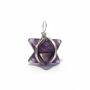 May include: A purple amethyst pendant in a star shape, wrapped with silver-colored wire. The pendant has a loop at the top for hanging. The background is white.