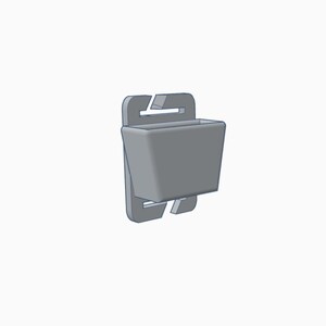 May include: A gray, 3D-rendered plastic clip-on container. The container has a rectangular shape with a small opening at the top. The clip has a hook and a slot for attachment. The design is simple and functional.