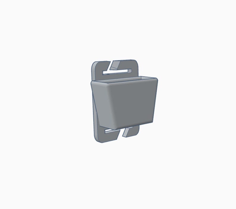 May include: A gray, 3D-rendered plastic clip-on container. The container has a rectangular shape with a small opening at the top. The clip has a hook and a slot for attachment. The design is simple and functional.