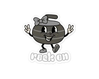 May include: A sticker featuring a cartoon curling stone with a bow, smiling and giving the peace sign. The text "rock on" is below the stone in a white outline.