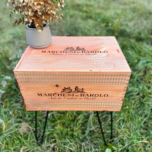 Può includere: Un tavolino in legno ricavato da una cassa di vino, con la scritta "MARCHESI di BAROLO Antiche Cantine in Barolo". Il tavolo ha gambe a forcina in metallo nero e una pianta decorativa in un vaso a righe.
