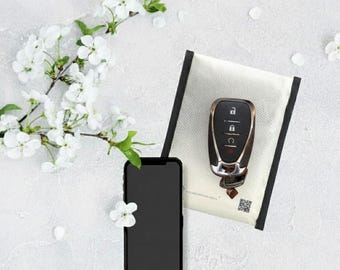 May include: A black smartphone and a car key fob rest on a white surface, next to a white pouch with a black border. White cherry blossoms and petals are scattered around the objects, creating a minimalist aesthetic.