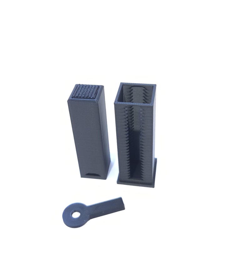 May include: Three black 3D-printed objects on a white background. There are two rectangular, hollow, vertical structures, one with a textured top. A small, flat, key-shaped object is also present.