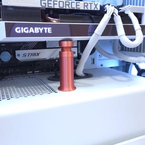 Peut inclure: Un objet cylindrique de couleur cuivr&eacute;e avec un dessus noir, possiblement un composant PC, se trouve devant une carte graphique d'ordinateur. La carte graphique porte l'inscription "GEFORCE RTX" et "GIGABYTE". Le bo&icirc;tier de l'ordinateur est blanc.