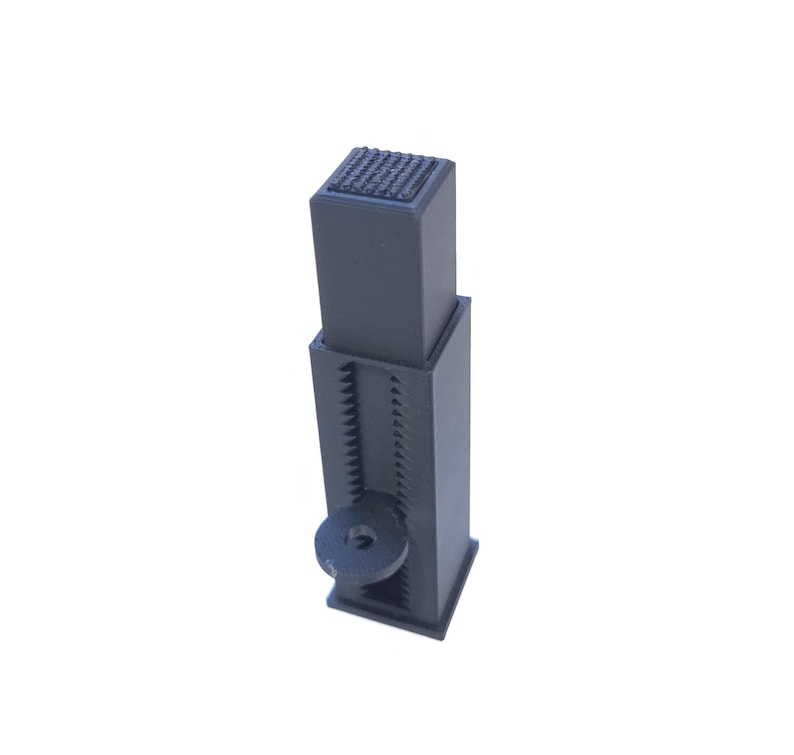 May include: A black adjustable furniture leg with a textured top and a circular adjustment knob. The leg has a square base and a series of teeth for height adjustment. The overall height is adjustable.