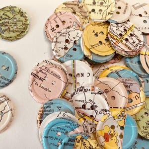 May include: Assortment of colorful map buttons with various locations and text printed on them. The buttons are made of paper and have a round shape.