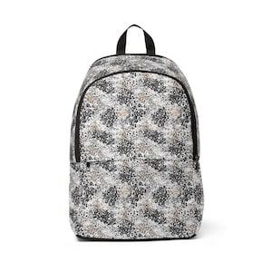 Può includere: Uno zaino con un motivo animalier ripetuto nei toni del nero, bianco e beige. La borsa presenta un ampio scomparto principale con chiusura a zip, una tasca frontale più piccola con zip e una maniglia superiore nera per il trasporto.