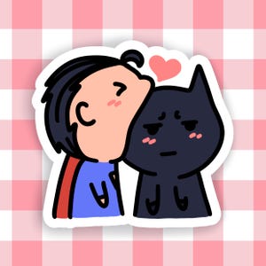 May include: A sticker featuring a cartoon illustration of a character in a blue shirt and red cape kissing a black cat-like figure. A pink heart floats above them, set against a pink and white checkered background.
