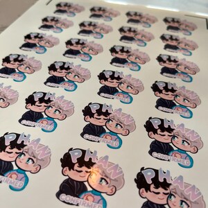 Puede incluir: Hoja de pegatinas con una ilustraci&oacute;n de dibujos animados de dos figuras abraz&aacute;ndose. Las figuras tienen cabello negro y claro, vistiendo trajes azules y negros. La palabra "PHAN" est&aacute; encima de ellos y "CONFIRMED" debajo.
