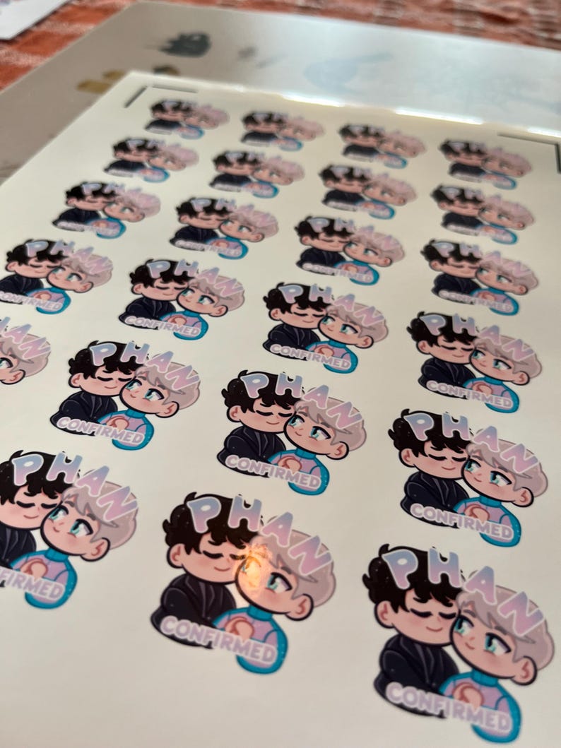 Puede incluir: Hoja de pegatinas con una ilustraci&oacute;n de dibujos animados de dos figuras abraz&aacute;ndose. Las figuras tienen cabello negro y claro, vistiendo trajes azules y negros. La palabra "PHAN" est&aacute; encima de ellos y "CONFIRMED" debajo.