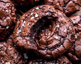 Peut inclure: Gros plan sur plusieurs cookies au chocolat noir avec une surface craquelée et saupoudrés de gros sel marin blanc. Les cookies sont d'une riche couleur marron et semblent fraîchement cuits, avec un aspect doux et texturé.
