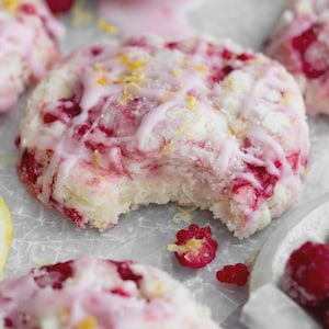 Peut inclure: Gros plan sur un scone aux framboises avec une bouchée. Le scone est garni d'un glaçage rose et de zeste jaune. Des framboises fraîches sont éparpillées autour du scone.
