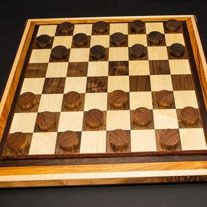 May include: A handcrafted wooden checkerboard with alternating light and dark squares. The board is framed with multiple wood tones and includes dark wooden checker pieces. The game board is set against a dark background.