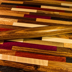 May include: A wooden rolling pin with a dark brown finish, lying on a colorful wooden cutting board made of various wood types.