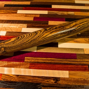 May include: A wooden rolling pin with a dark brown and black striped pattern. The rolling pin is lying on a colorful wooden surface.