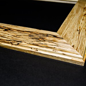 Op de afbeelding: Close-up van een houten fotolijst met een natuurlijke houten afwerking. De lijst heeft een uniek houtnerfpatroon en een lichtbruine kleur.