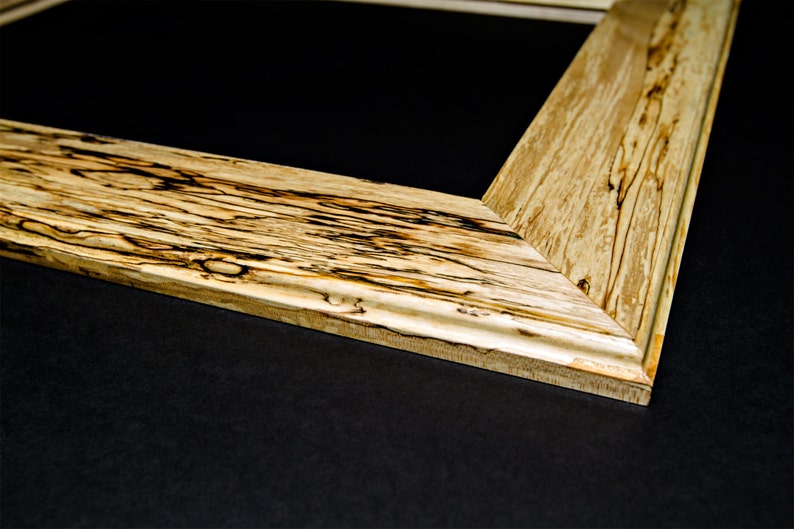 Op de afbeelding: Close-up van een houten fotolijst met een natuurlijke houten afwerking. De lijst heeft een uniek houtnerfpatroon en een lichtbruine kleur.