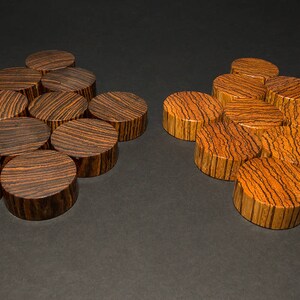 May include: Two sets of wooden plugs with a striped grain pattern. One set is dark brown, the other is a lighter orange-brown. The plugs are arranged in small clusters on a dark surface. These decorative plugs are likely for jewelry.