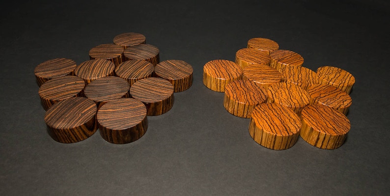 May include: Two sets of wooden plugs with a striped grain pattern. One set is dark brown, the other is a lighter orange-brown. The plugs are arranged in small clusters on a dark surface. These decorative plugs are likely for jewelry.